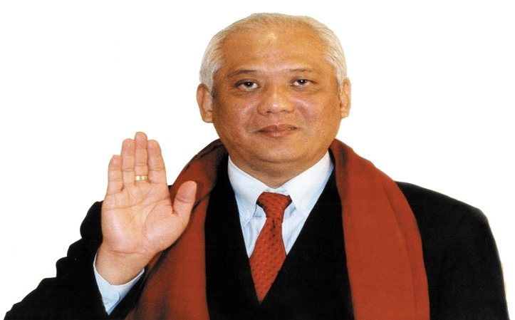 Grand Master Choa Kok Sui in a dark suit with a red scarf, right hand raised in blessing