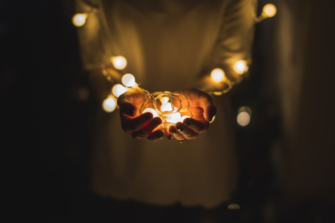 Cupped hands holding a warm glow of light against a dark background