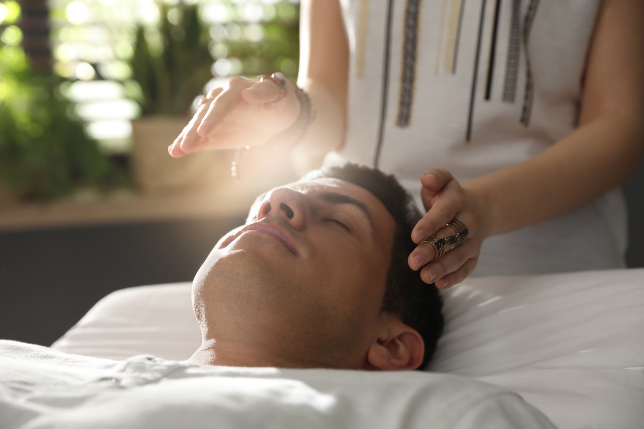 A practitioner's hands held above a person resting calmly with eyes closed during an energy healing session